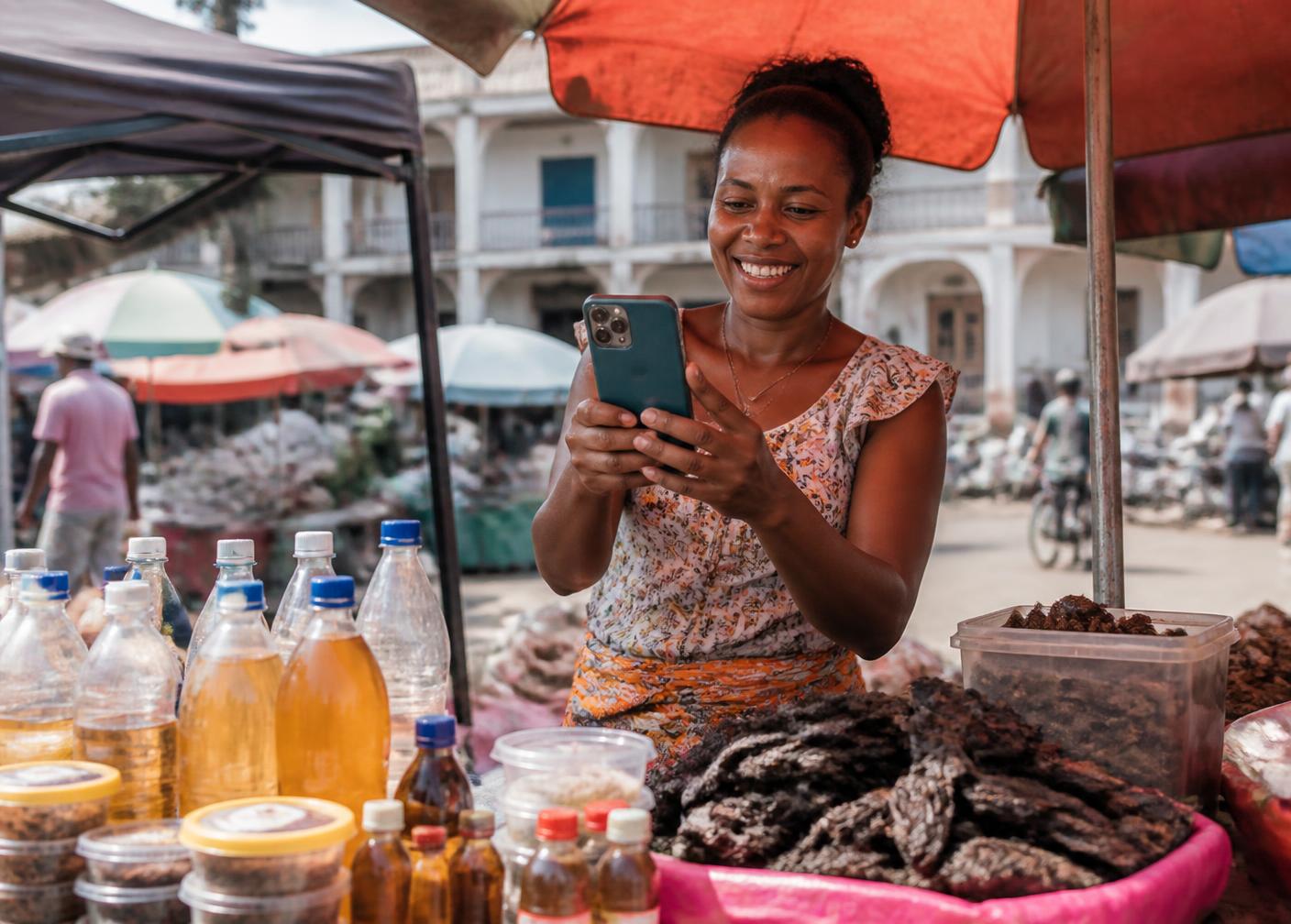 Vendeuse malgache utilisant son smartphone pour promouvoir ses produits au marché